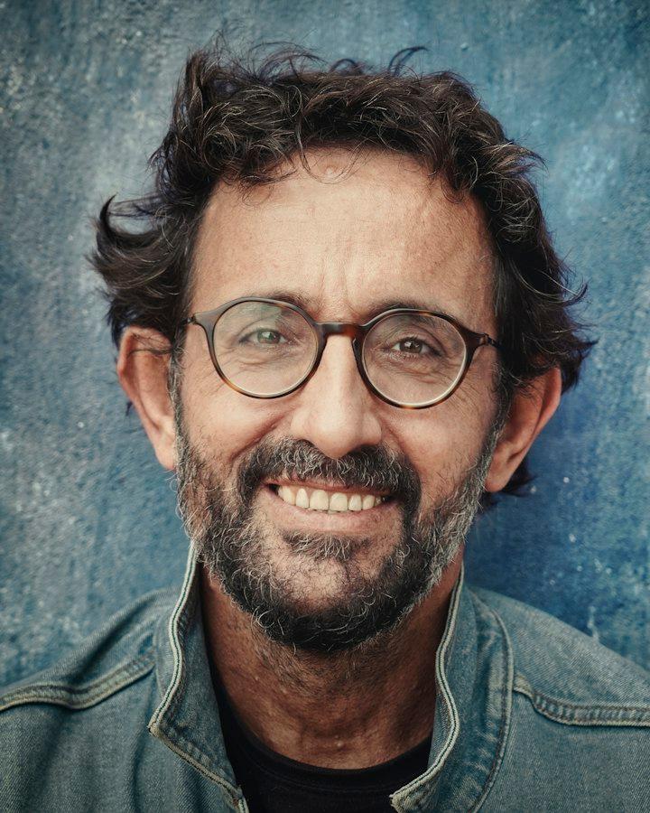 An older man with glasses and a grey beard, smiling